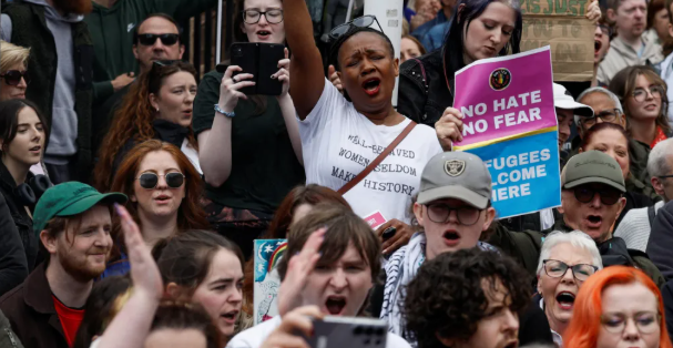 Crowds of anti-racism protesters gather in Belfast, chanting and holding signs reading “No Hate No Fear” and “Refugees Welcome Here” during a demonstration against racism and anti-immigrant violence.