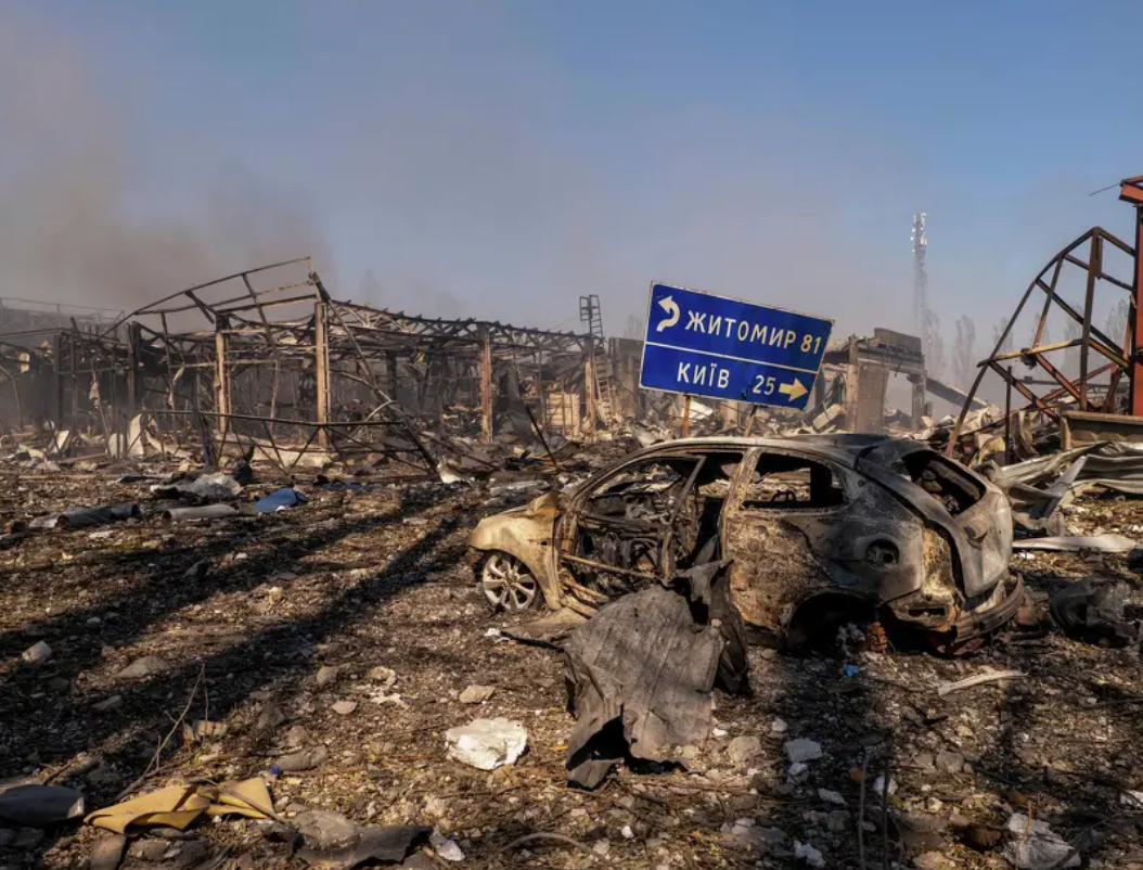Burned car and destroyed warehouse buildings beside a road sign pointing towards Kyiv and Zhytomyr in Myla, Ukraine
