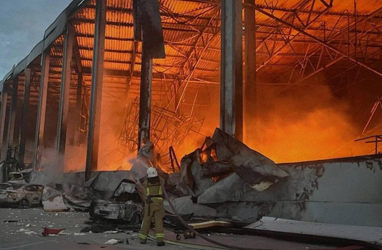 A firefighter directs a hose towards flames inside a badly damaged warehouse near Kyiv