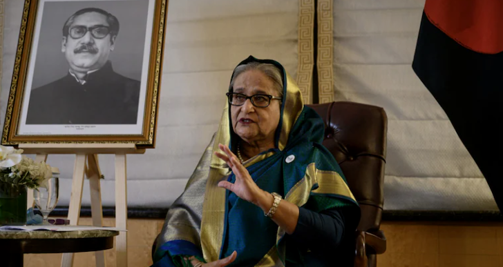 Former Bangladesh Prime Minister Sheikh Hasina speaking beside a portrait of Sheikh Mujibur Rahman and the Bangladesh flag