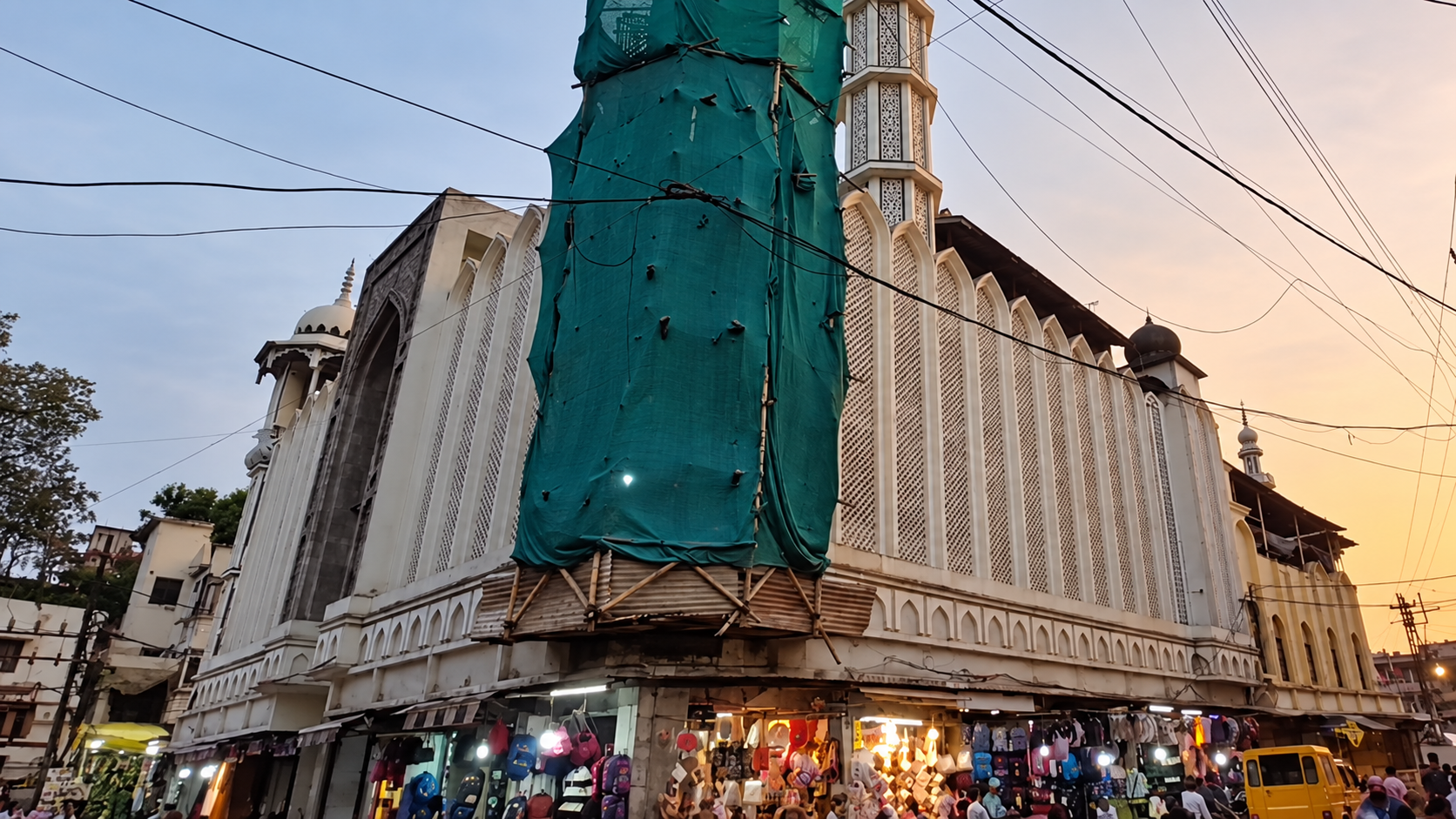 Exterior of the Shahi Masjid in Ujjain, with green sheeting around one section and shops at street level