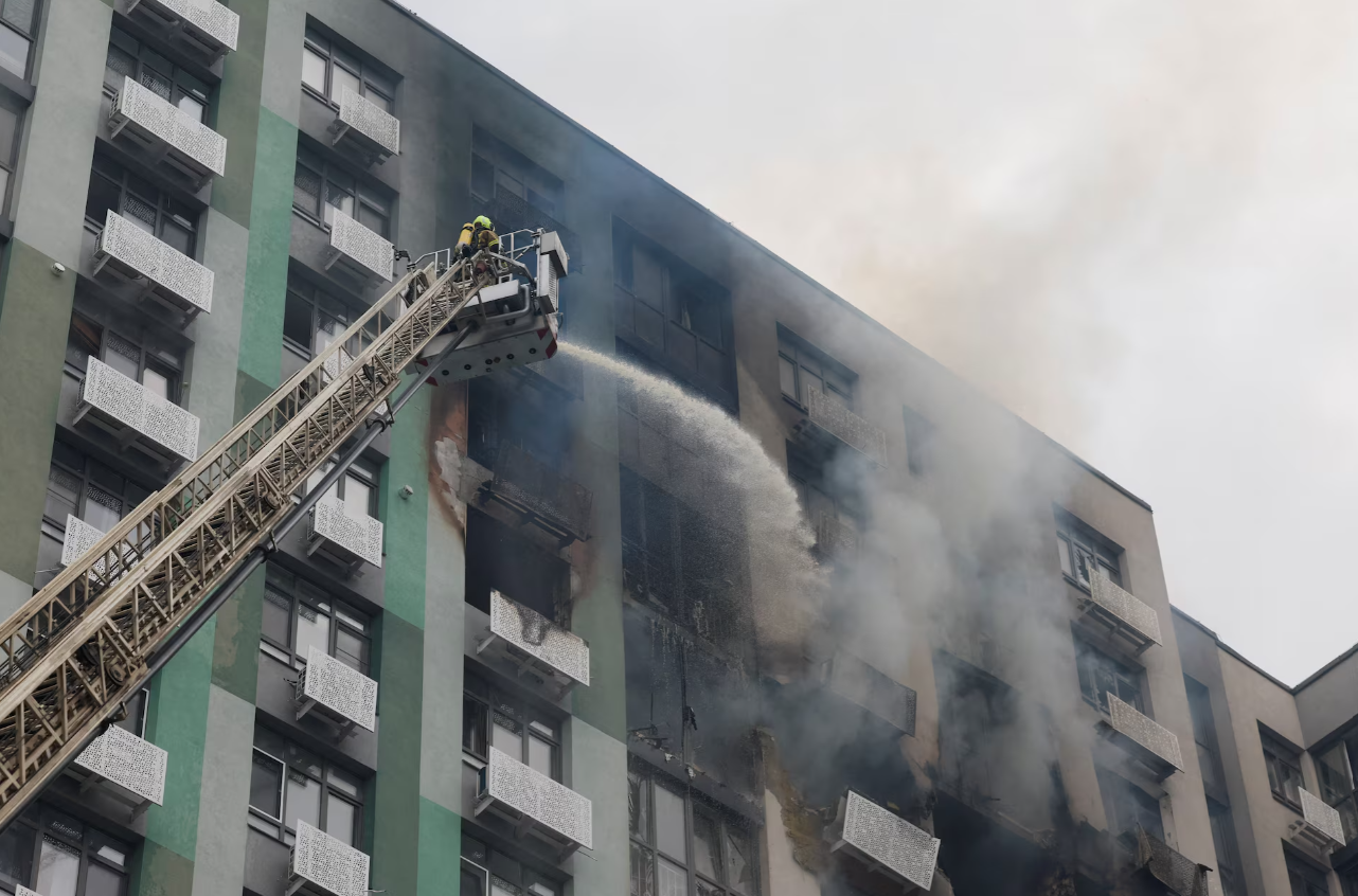 A firefighter sprays water from an aerial platform onto a drone-damaged apartment building in Kyiv