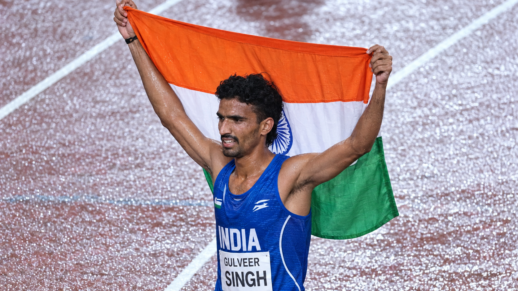 Gulveer Singh raises the Indian tricolour above his head on the athletics track.