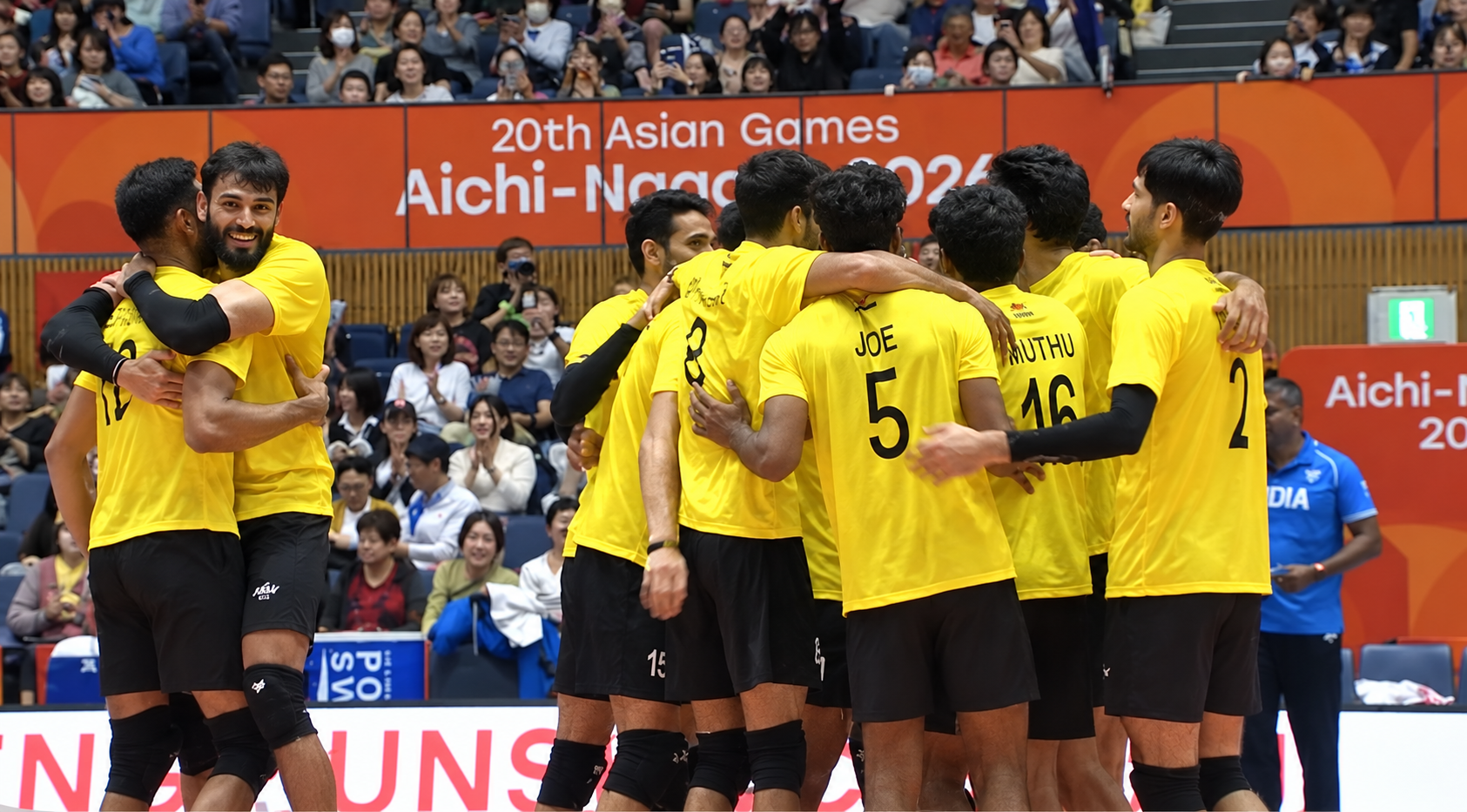 Indian men’s volleyball players in yellow jerseys embrace and celebrate.