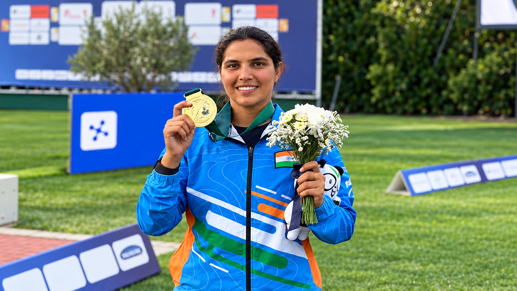 Neeru Dhanda smiles while displaying her gold medal and holding a bouquet in India’s blue team jacket.