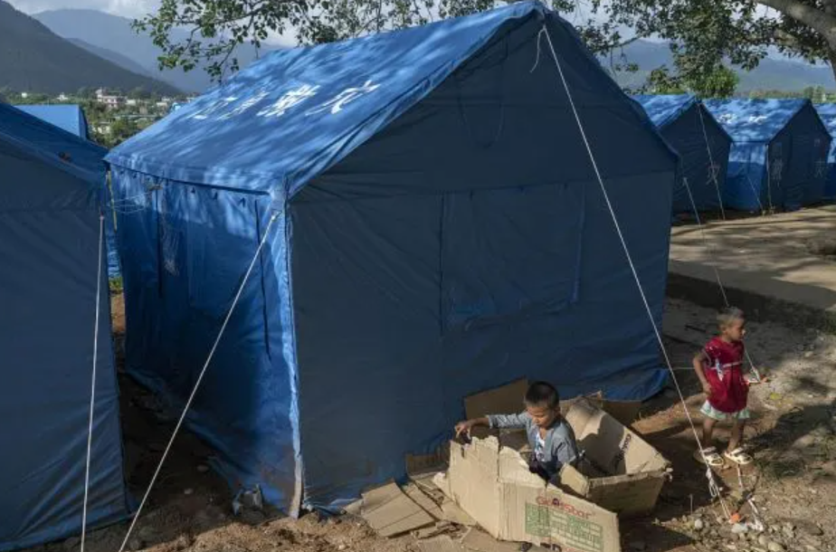 Children beside rows of blue temporary shelter tents for flood-affected families in Nepal