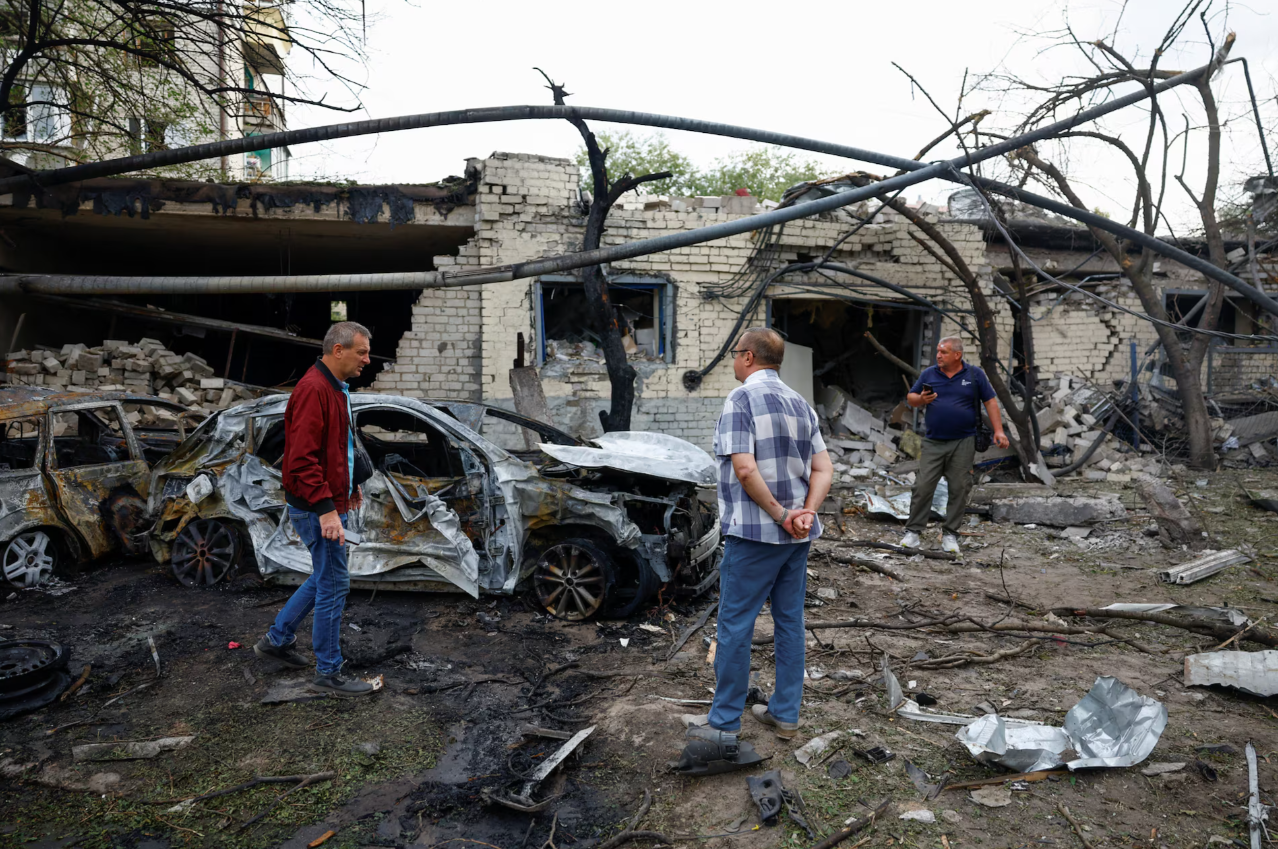 Residents stand beside burned cars and a ruined building following a Russian missile strike in Boryspil