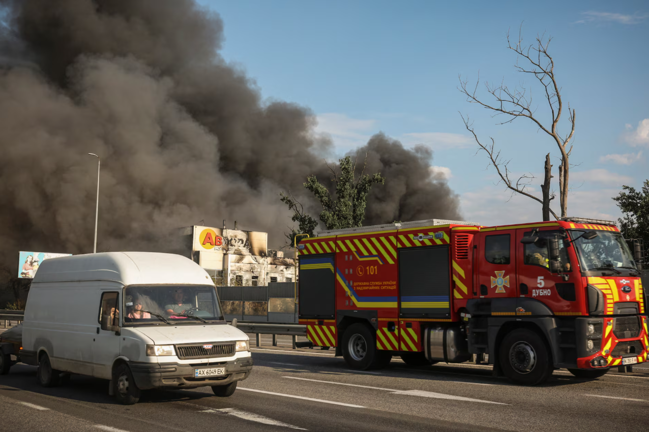 A firetruck and van pass a burning warehouse as black smoke rises in Ukraine's Kyiv region